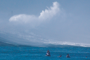 Fume rising into the sky as a large wave breaks over on the far side of the bay at Waimea.